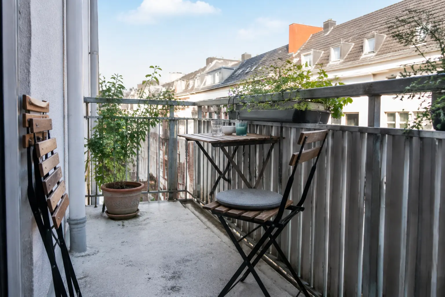 Schmaler Balkon mit an die Wand geklapptem Tisch und zwei leichten Klappstühlen